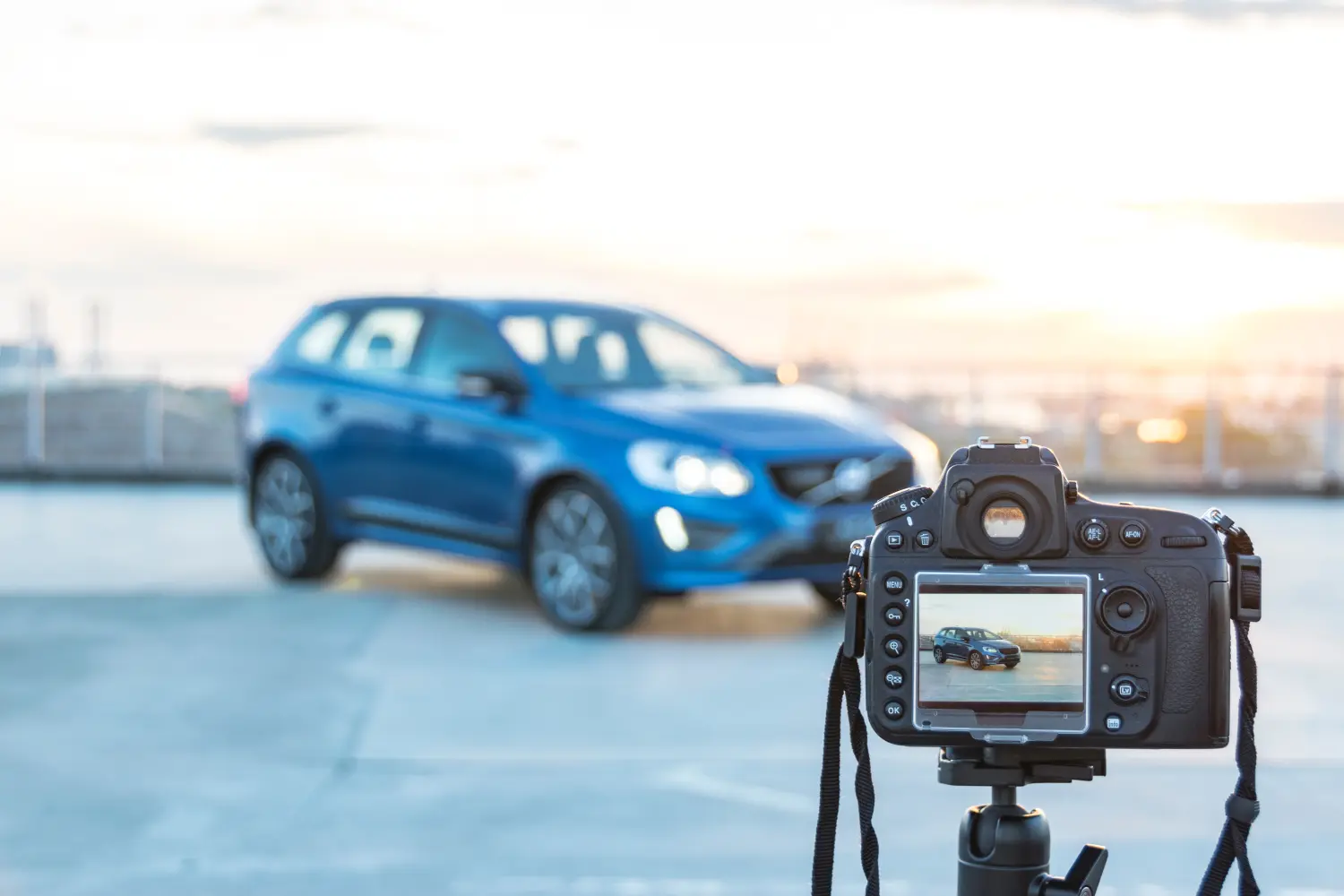 Eine Fotokamera fotografiert ein modernes Auto auf dem Dach eines Gebäudes bei Sonnenuntergang